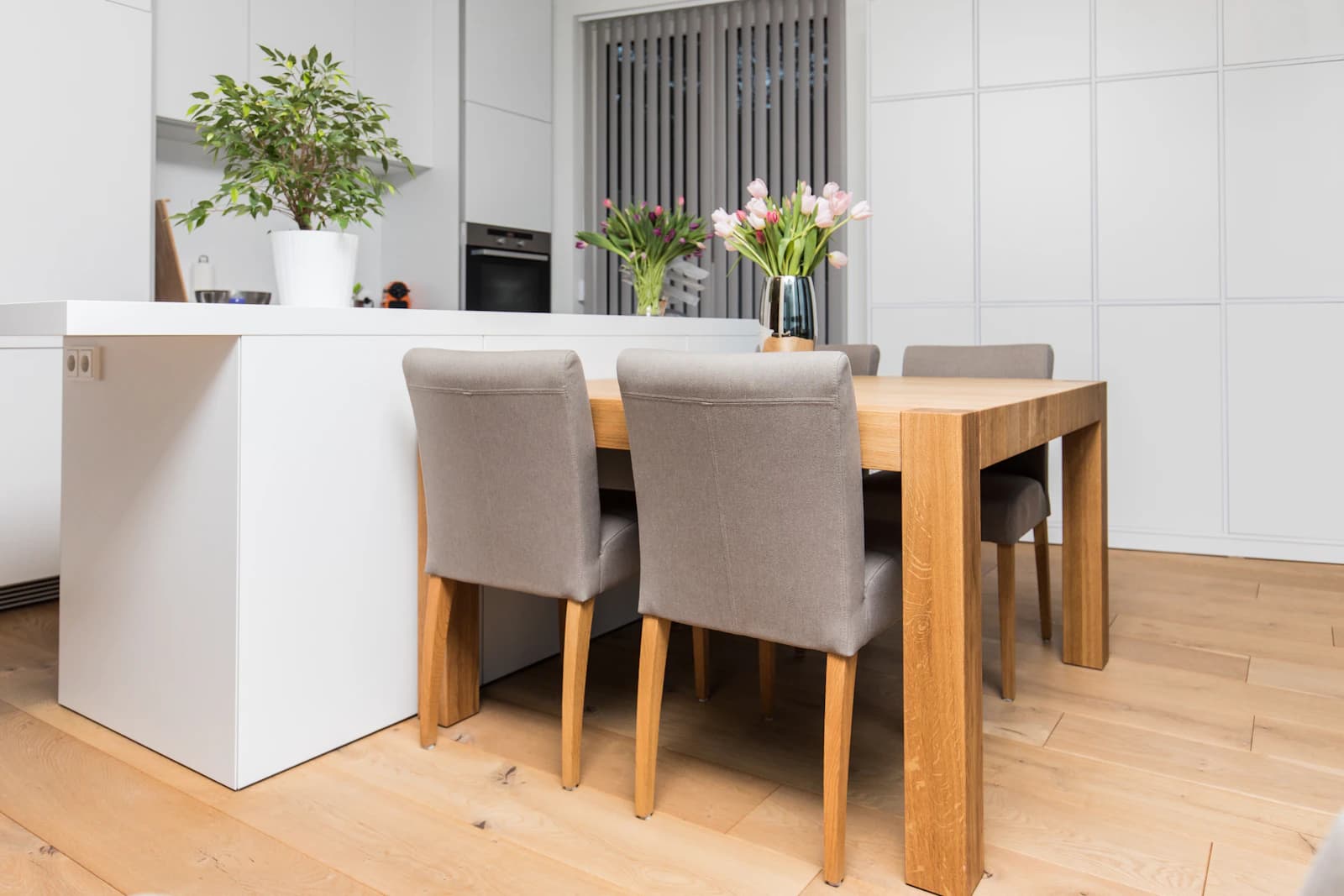 Ljust och lugnt kök och matplats med träbord, stolar och blommor